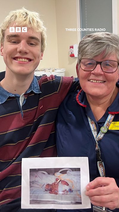 Tall teenager with blond hair stands next to neonatal nurse that looked after him when he was born