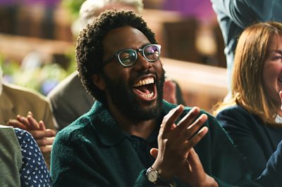 Un personaje llamado Gus (Daniel Lawrence Taylor) se ríe y aplaude.