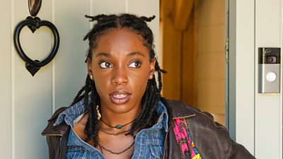 Una mujer (Leah, Boarders) con una mochila entra por una puerta.