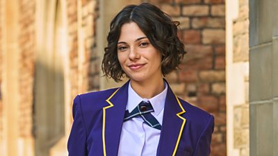 Una joven estudiante (Pixie en Boarders) posa con un uniforme morado.