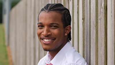 Un hombre (Benjamin de Boarders) con un pendiente sonríe fuera de una valla.