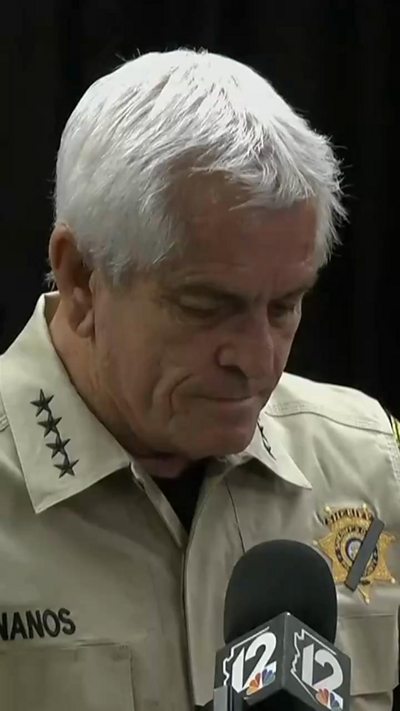 A Sheriff wears a uniform with his head bowed while speaking to the media behind a microphone.