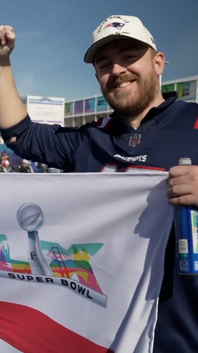 A patriots fan is holding a flag with his fist in the air.