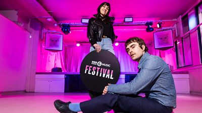 Two people in a pink venue with branding for the BBC Radio 6 Music Festival. 
