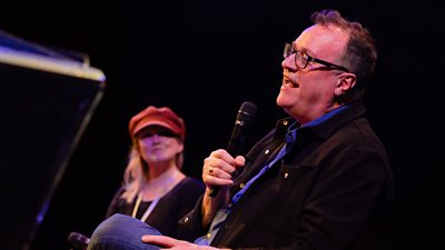 The writer Russell T Davies speaking into a microphone during a Q&A with author Terri White in the background