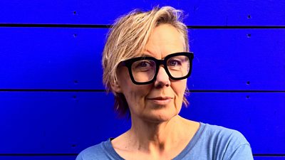 A woman stands in front of a blue background