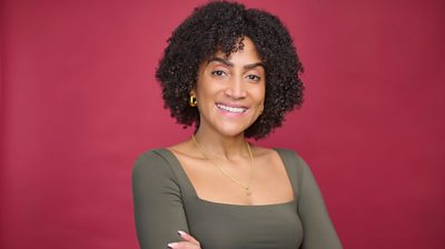A woman looks at the camera against a pink background