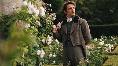 A man stands in a garden beside white flowers. 