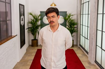 A man (Phil Wang) in a white shirt stands in a hallway.