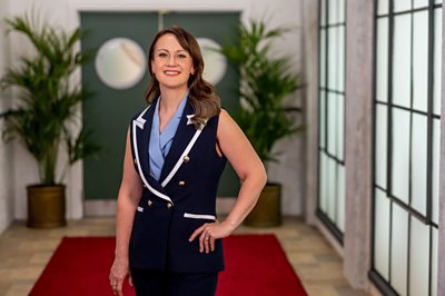 A woman (Lorna McNee) in a smart waistcoat poses in a hallway.