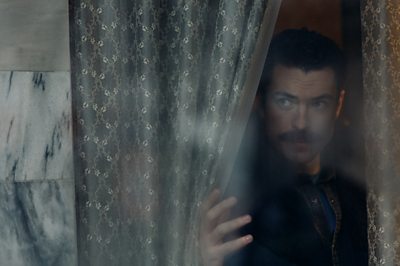 A man looks through a curtain.