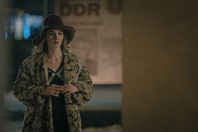 A woman in a fur coat and a leopard print hat looks into the distance. 