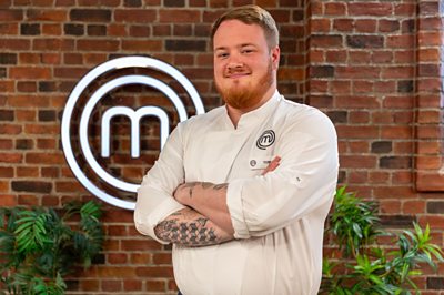 A man in a chef uniform stands in the MasterChef studio with the name badge TOM.