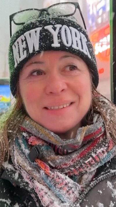 Woman in a new york hat speaks while covered in snow.