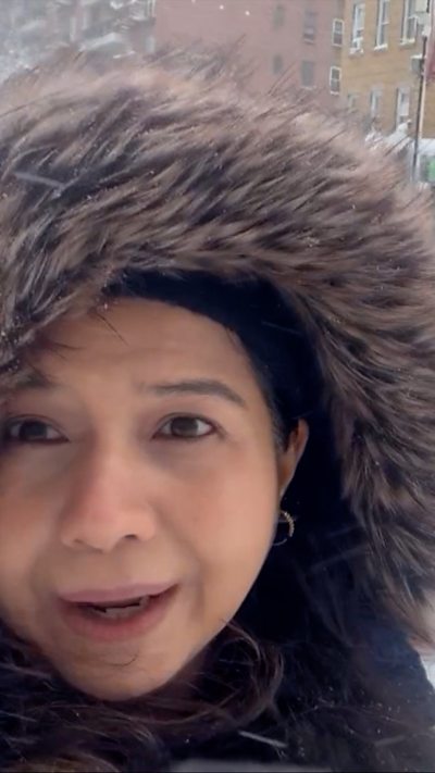 A woman is outside wearing a fluffy rimmed coat looking at the camera.