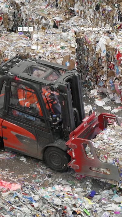 Red and black truck pushing rubbish in a recycling centre, driver is wearing an orange and white high viz