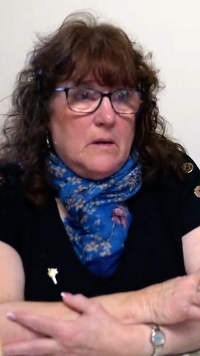 Llun o fenyw yn eistedd i lawr gyda'i breichiau wedi'u croesi yn edrych yn ofidus