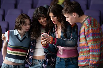 A group of young people check something on someone's phone.