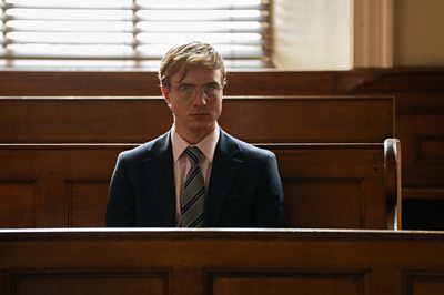 A man in a suit sits in a courtroom.