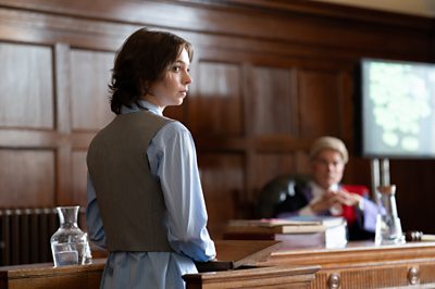 A young woman looks concerned in a court while a judge sits in the backdrop.