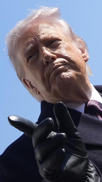 Donald Trump wears a dark overcoat and points a gloved finger toward a reporter.