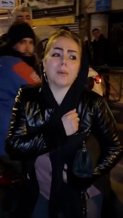 A woman clutches her chest on a street in Tehran