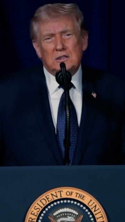 A man with grey hair in a suit stands at a podium.