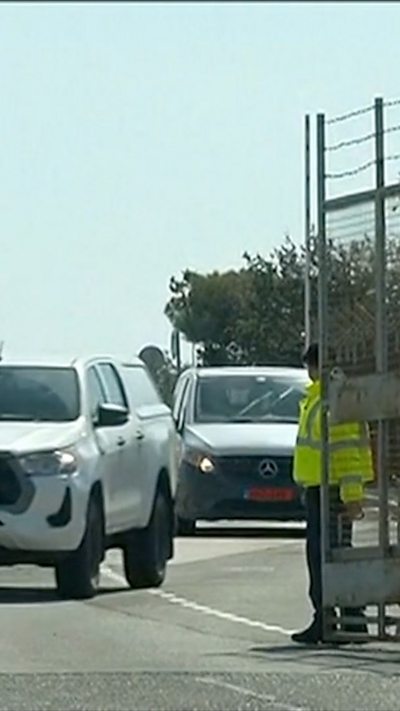 White cars drive out a gate help open my man wearing reflective jacket