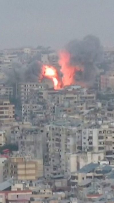 A fiery red explosion in the middle of buildings with smoke rising above the city of Beirut