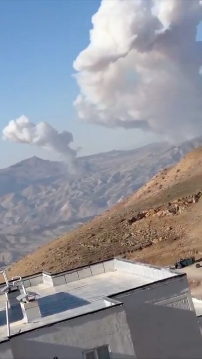 Smoke rises in plumes into a blue sky over hills