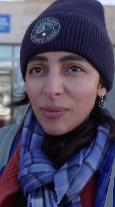 A young woman speaks to the camera, she wears a beanie and scarf