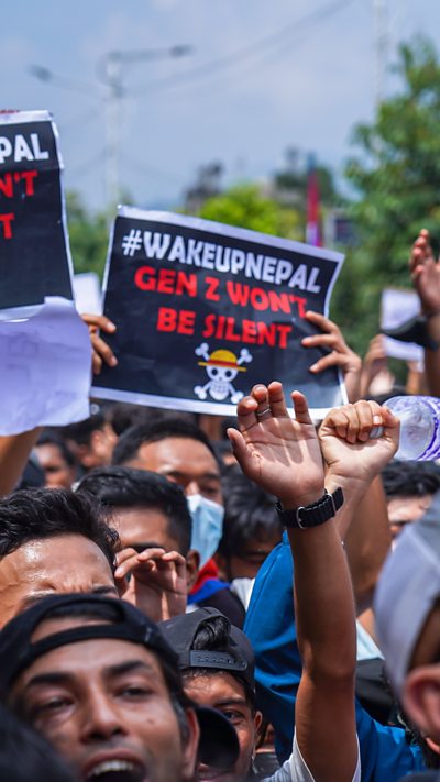 Protesters in the streets of Kathmandu, Nepal. One is holding a sign that reads #WAKEUPNEPAL Gen Z Won't Be Silent