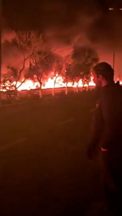 A man looks on as flames illuminate a street set alight by spilled oil