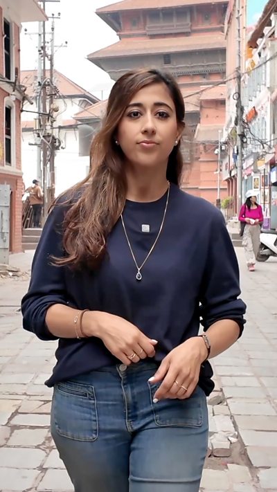 Woman wearing blue jumper and jeans walking in down a street in Nepal