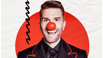 Photo of Joel Dommett smiling and wearing a red nose in front of branding for Red Nose Day 2026. 