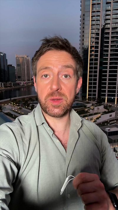 BBC Correspondent Nick Beake wearing polo shirt and holding headphones with mic