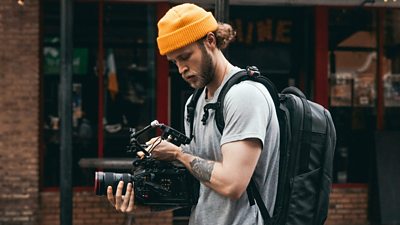 A content creator is in a street scene, filming with a camera.