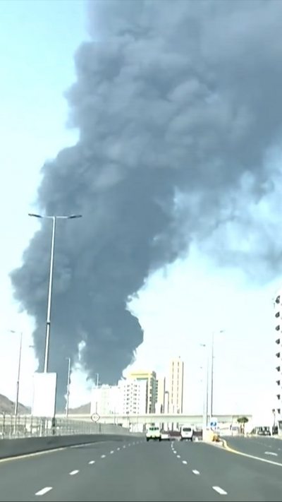 Two huge dark grey plumes of smoke can be seen rising above what looks like a motorway