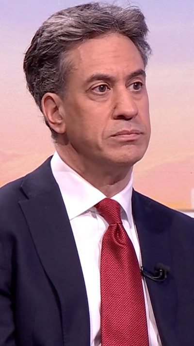 Ed Miliband sitting in a BBC studio, wearing a dark navy blue suit jacket, white shirt and red tie.