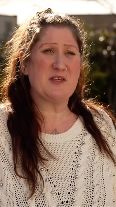 Khali Goodwin, who has brown hair and wears a white jumper, speaks to the camera