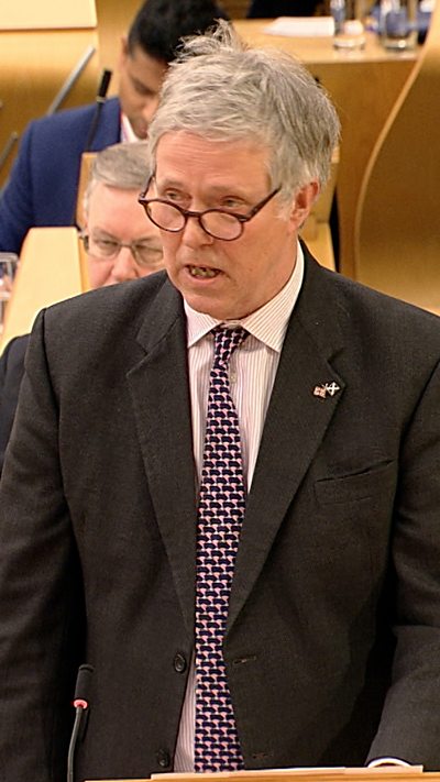 Man in dark suit and patterned tie in Scottish Parliament chamber