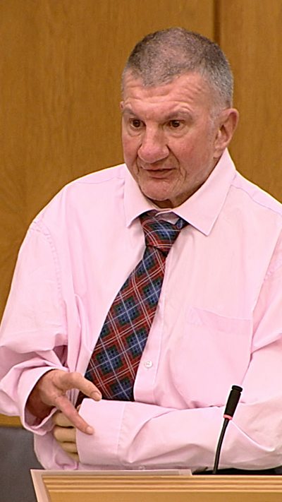 A man in a pink shirt and tartan tie in the Scottish Parliament chamber