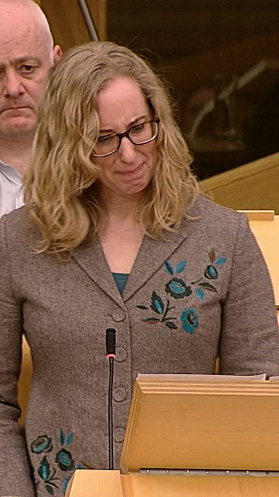A woman in a grey jacket in the Scottish Parliament chamber.