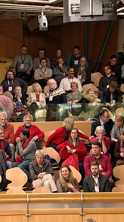 Crowds of people on rows of seats in the Scottish Parliament chamber.