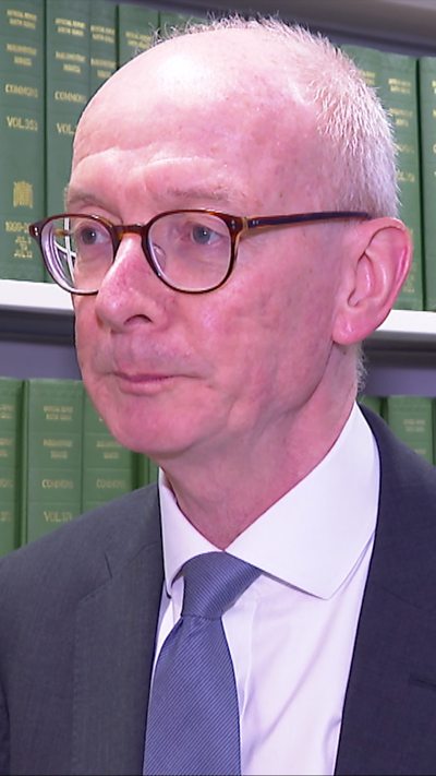 Man in a suit and tie with white hair, standing in front of shelves filled with green law books.