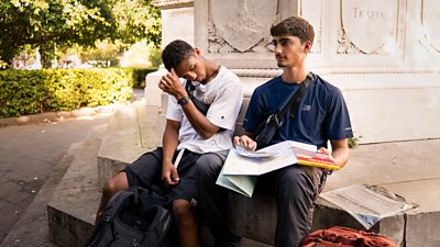 Two young men sit on the steps of a monument looking slightly tired and confused. They hold a map.