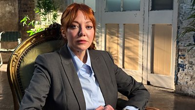 Diane Morgan in character as Philomena Cunk sits in an armchair. 