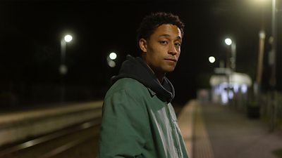 Photo of Ben Coyle-Larner in character as Arran. Stood on a station platform. 