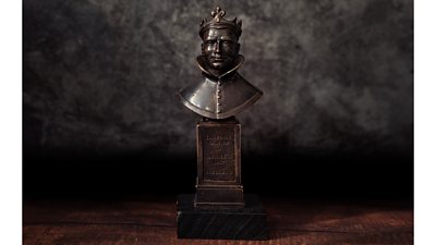 An awards statueette featuring a bust of a man's head, featuring a crown and large collar