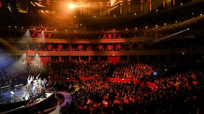 A wide shot featuring a group of performers on stage, performing for a packed Royal Albert Hall